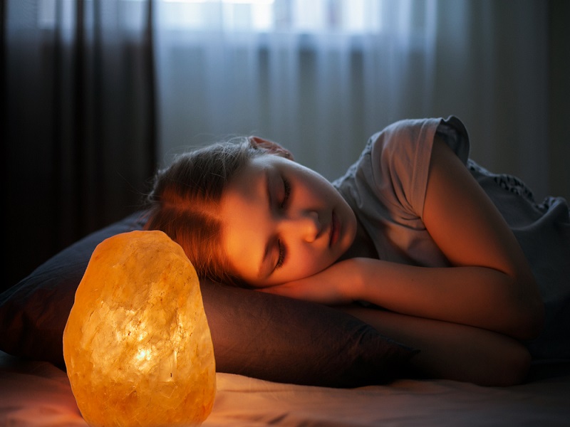 In this image show a girl sleeping with himalayan salt lamp